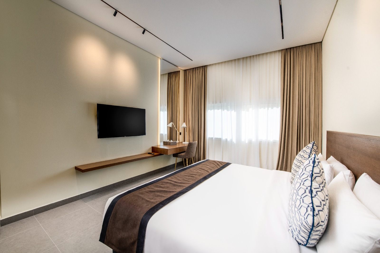 Bedroom with wall-mounted TV, desk and sheer curtains